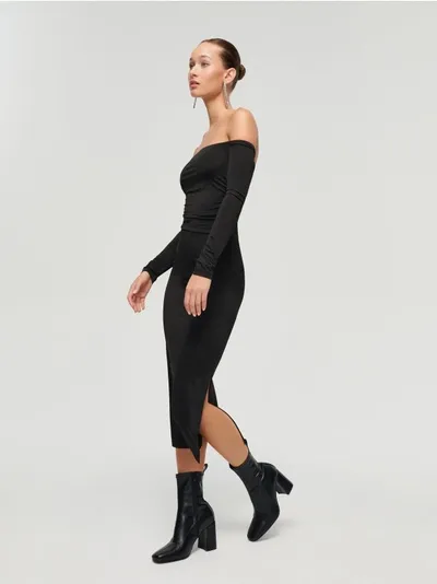 Czarna sukienka midi z odsłaniającym obojczyki dekoltem. Dopasowana, dzianinowa sukienka z dekoltem off shoulder. Model z długimi rękawami — całość projektu uzupełnia drapowanie. Modelka prezentuje produkt w rozmiarze: S/36Wzrost modelki 172 cm - czarny