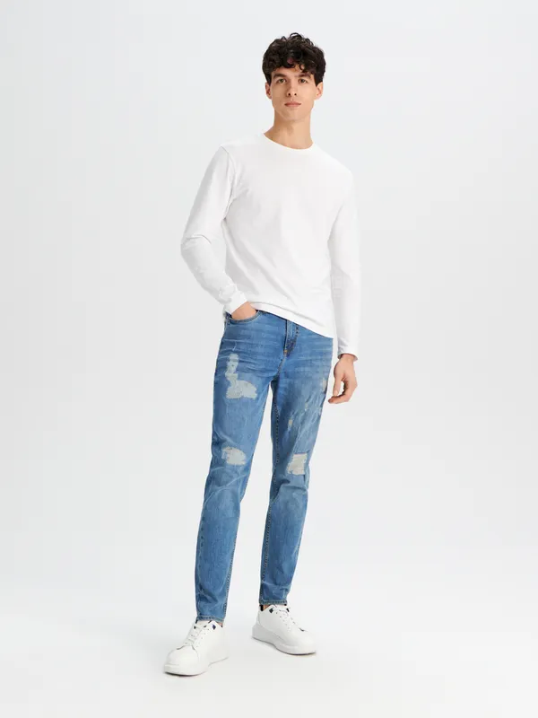 Spodnie jeansowe z ozdobnymi przetarciami na nogawkach uszyte z bawełny z dodatkiem elastycznych włókien. - niebieski