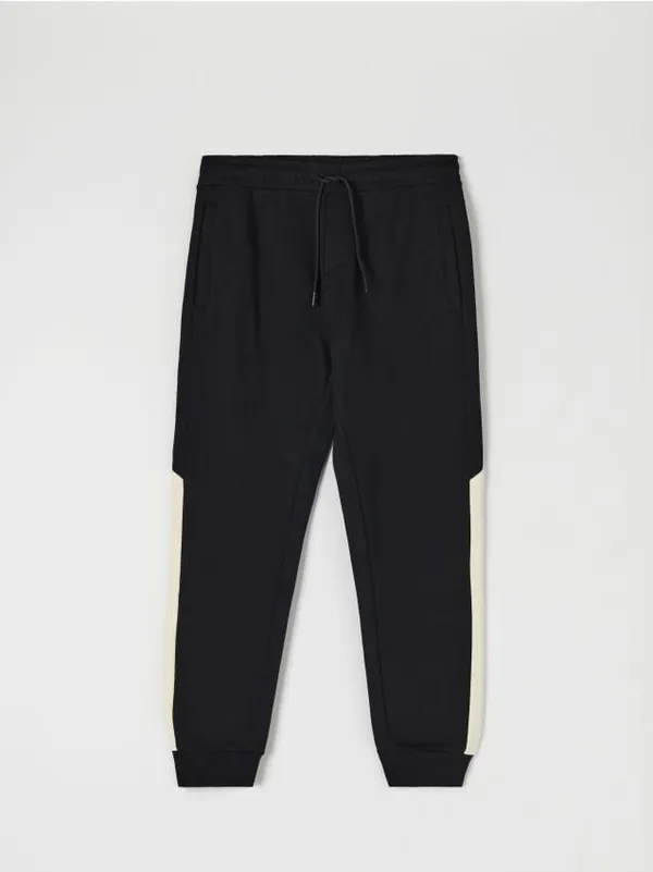 Bawełniane spodnie dresowe o kroju regular jogger, wykończone ściągaczami. Łączone kolory na nogawkach. - czarny